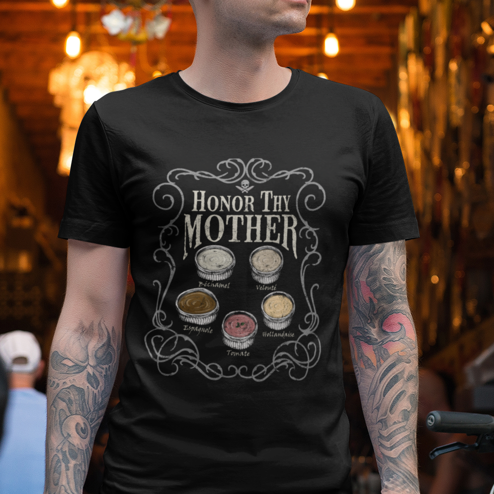 A man wearing a black graphic t-shirt with the text 'HONOR MY MOTHER' and illustrations of coffee cups, standing in a busy, warmly lit coffee shop.