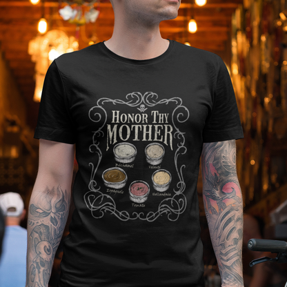 A man wearing a black graphic t-shirt with the text 'HONOR MY MOTHER' and illustrations of coffee cups, standing in a busy, warmly lit coffee shop.