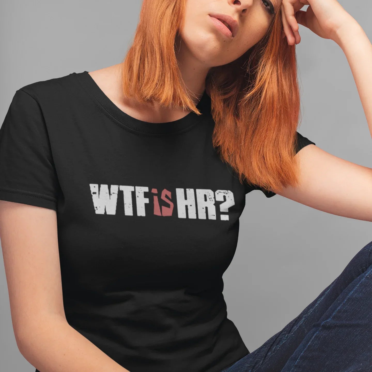 Person wearing a black t-shirt with 'WTF IS HR?' text, sitting against a gray background