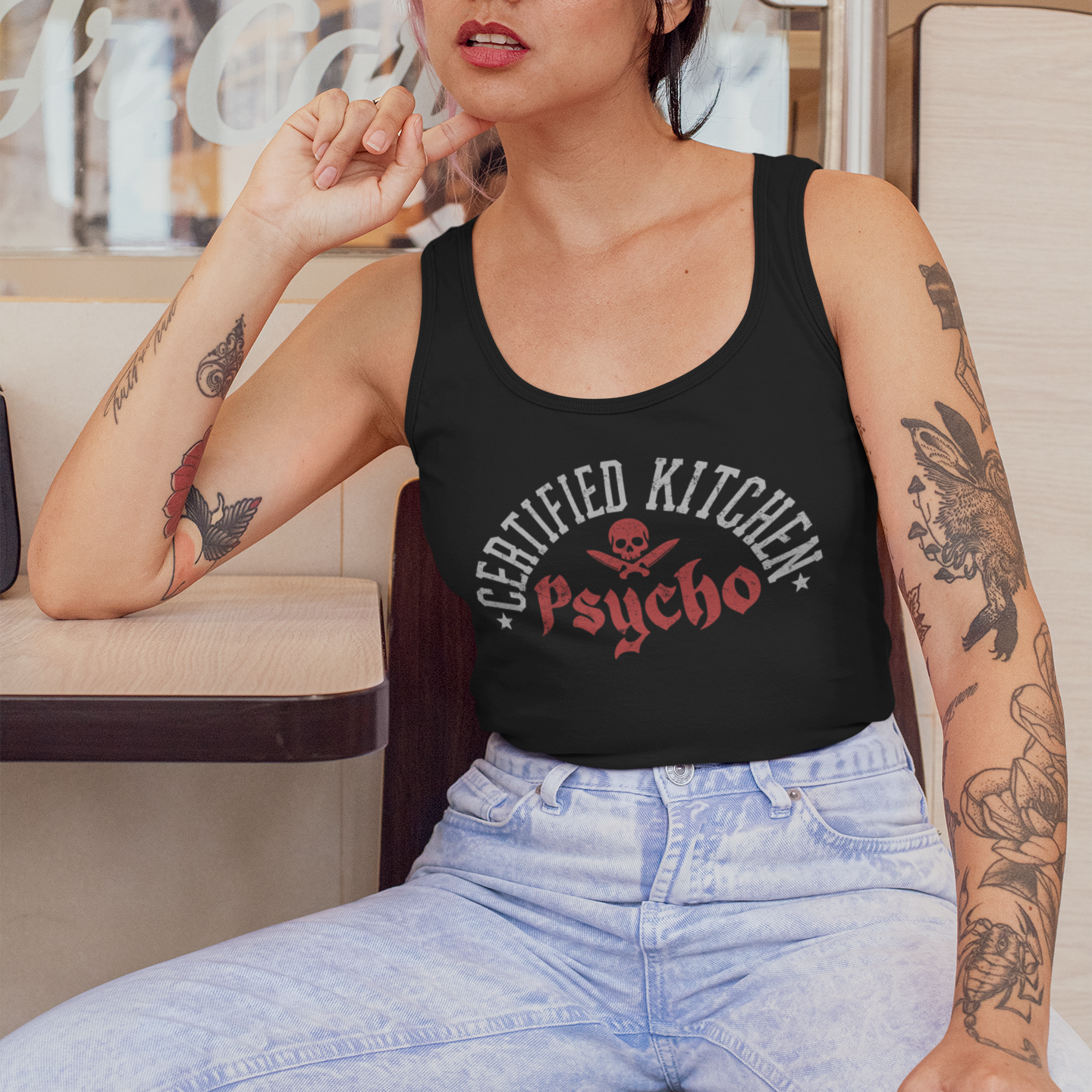 Woman wearing a black tank top with 'Certified Kitchen Psycho' text, sitting in a vehicle.