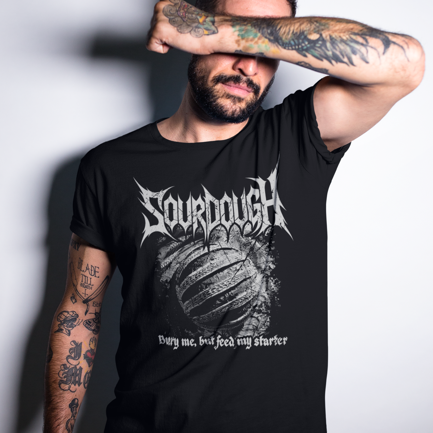Man wearing a black t-shirt with 'Sourdough' design, covering his face with his arm.