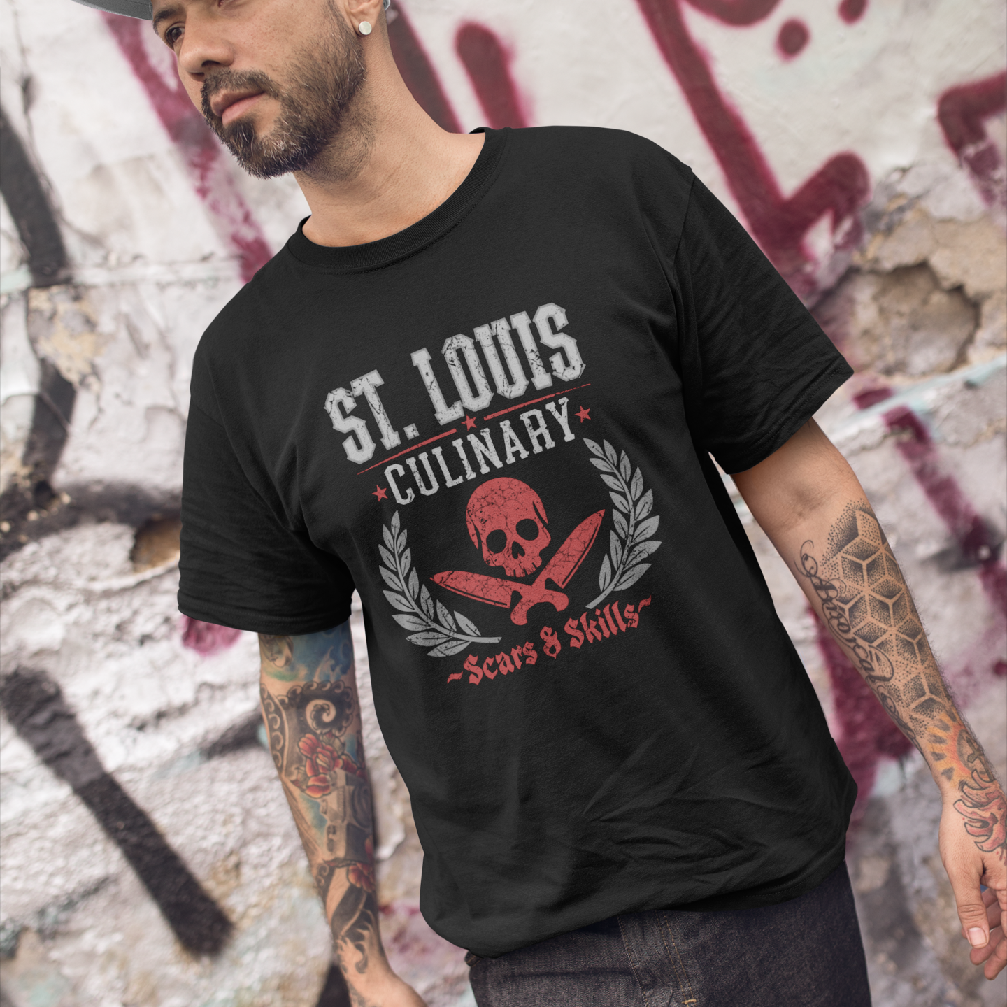 Man wearing a black t-shirt with 'St. Louis Culinary' design against a graffiti-covered wall.