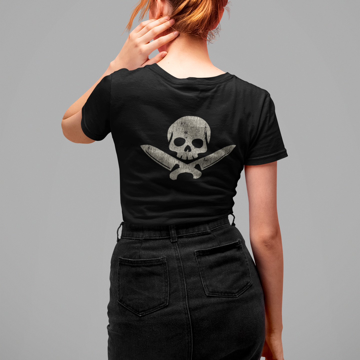 Person wearing a black t-shirt with a skull and crossbones design on the back, standing against a gray background.