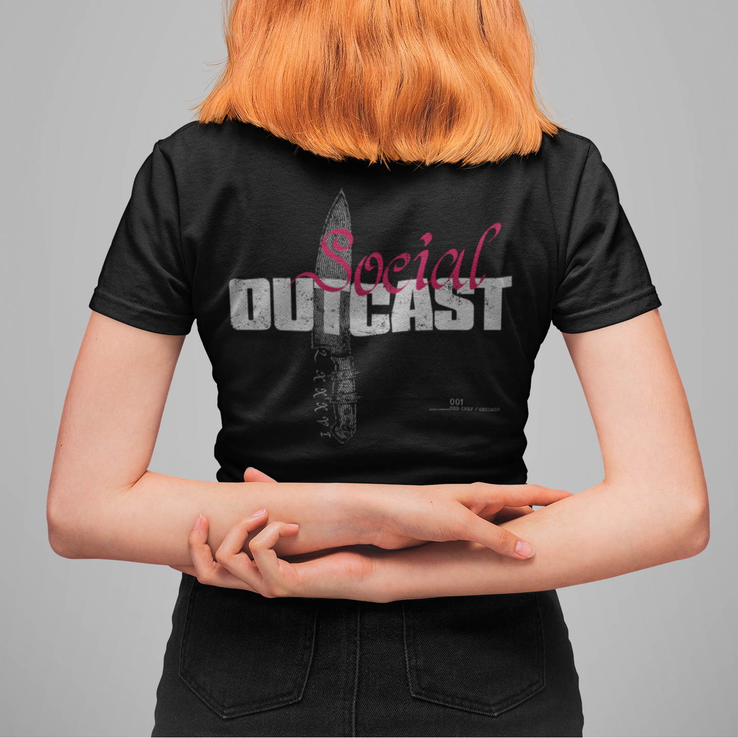 A person shown from the back wearing a black short-sleeve T-shirt with a large graphic print on the back. The shirt features the word 'Social' in pink script and 'OUTCAST' in distressed white block letters over a knife illustration.