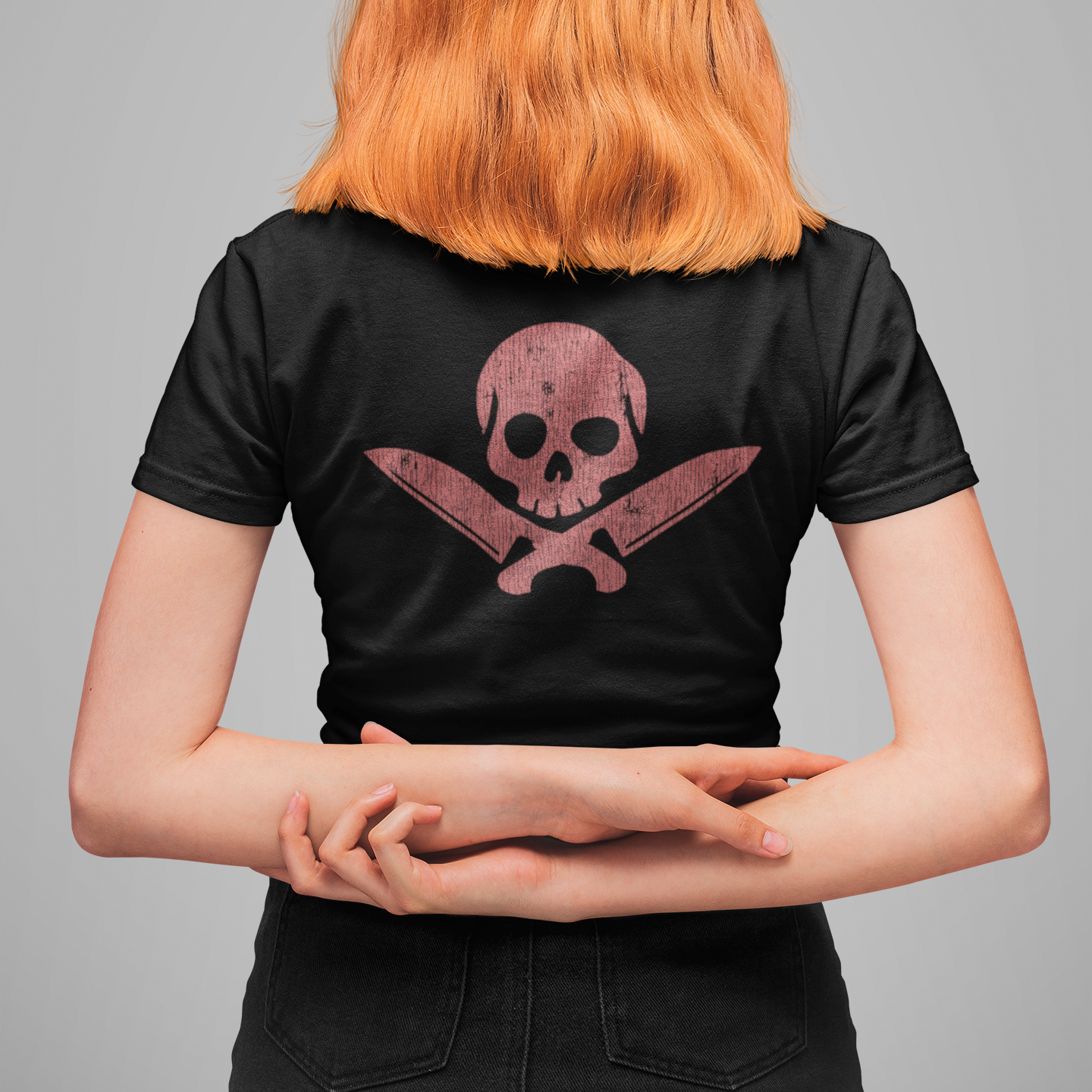 Person wearing a black t-shirt with a pink skull and crossbones design on the back, standing against a gray background.