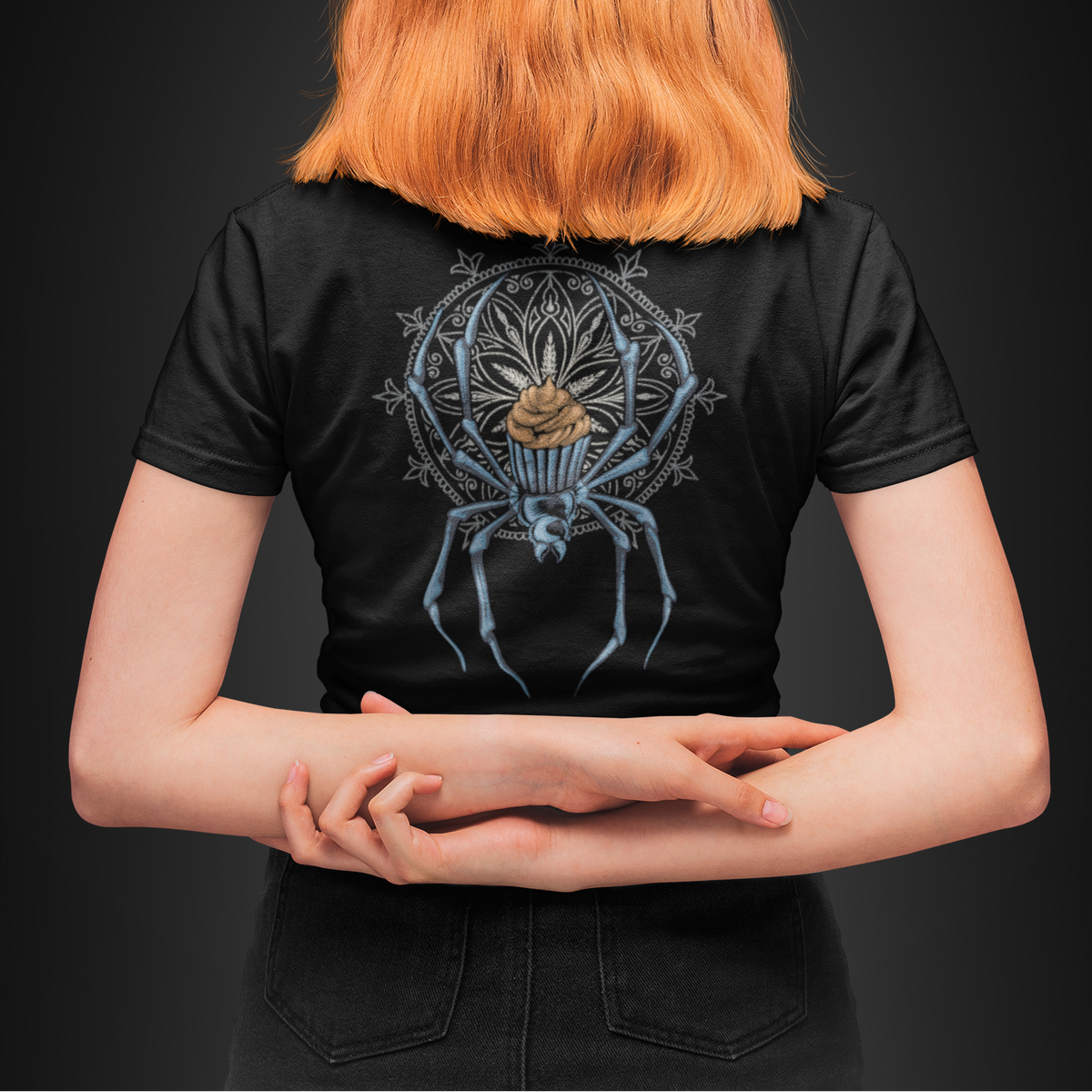 A person viewed from behind wearing a black short-sleeve T-shirt with a large detailed spider graphic on the back, set against a dark studio background.