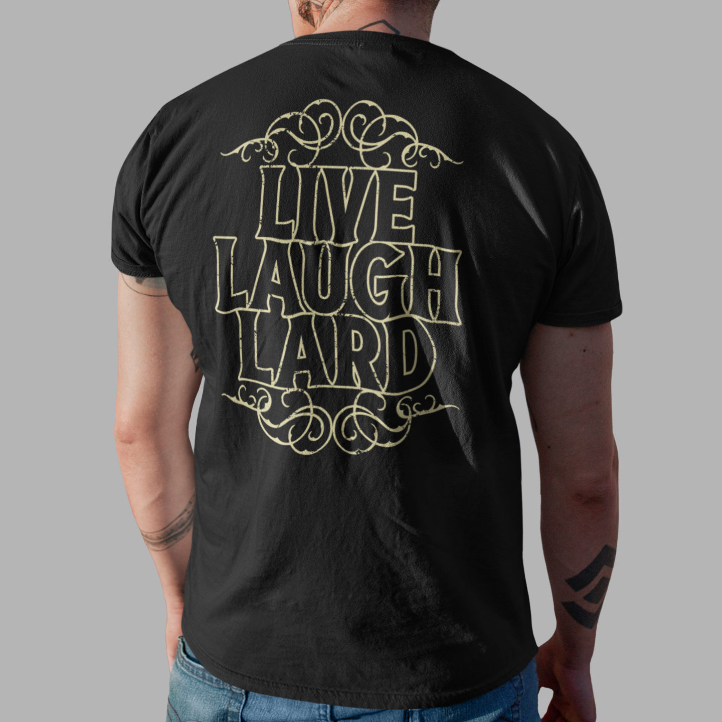 A man viewed from behind wearing a black t-shirt with a gold graphic that reads 'LIVE LAUGH LARD' and blue jeans, set against a solid gray background.