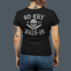 Person wearing a black t-shirt with text and skull design on the back, standing against a dark background.