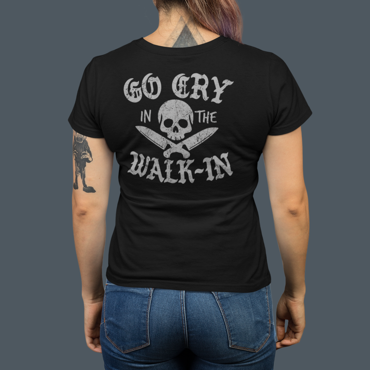 Person wearing a black t-shirt with text and skull design on the back, standing against a dark background.