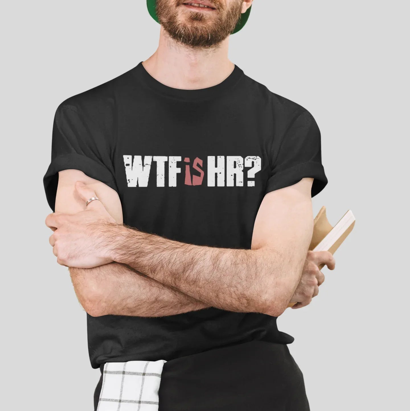Man wearing a black t-shirt with 'WTF is HR?' text, holding a pencil and notebook against a gray background